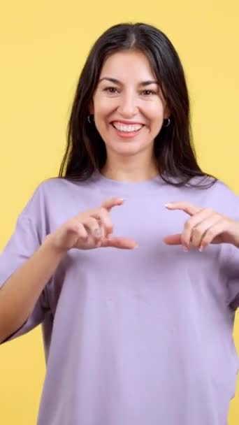 黄色の背景を持つスタジオで指の形をした心を表す女性 — ストック動画