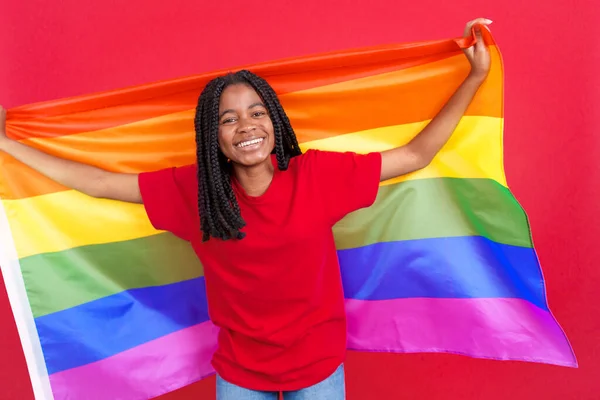 stock image Happy african woman raising a lgbt rainbow flag in studio with red background