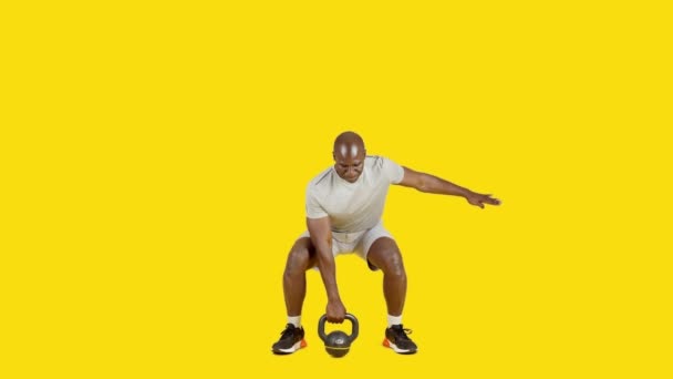 一个有着黄色背景的工作室里的视频是一个非洲的体育男子和Kettlebell一起做交替蹲 — 图库视频影像