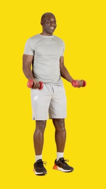 一个非洲男人用哑铃做卷曲二头肌的带黄色背景的工作室录像 — 图库视频影像