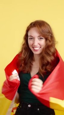 Stüdyoda sarı arka planda İspanyol bayrağıyla sarılan mutlu kızıl saçlı kadın.