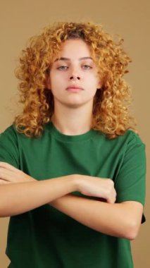 Studio video of a young woman with curly hair crossing the arms while looking at camera with an angry expression