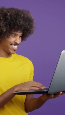 Happy african man wit curly hair standing and using a laptop in studio