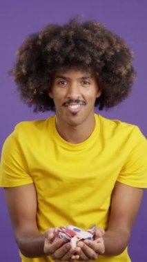 Cool african man with curly hair surrounded by multicolored confetti flying in the air in studio