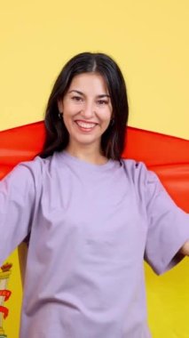 Happy caucasian woman wrapping with a spanish national flag in studio with yellow background