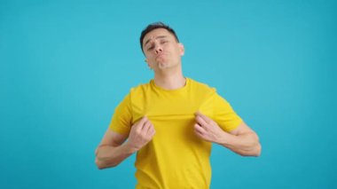 Stüdyoda, beyaz bir adamın mavi arkaplanlı ve baskıcı bakışlarıyla kameraya bakan bir video var.