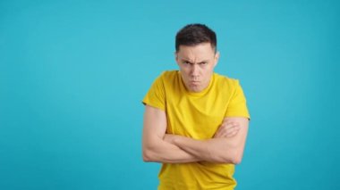 Stüdyoda, kollarını kavuşturmuş, çocuksu bakışlarla kaşlarını çatan öfkeli bir adamın mavi geçmişiyle video.