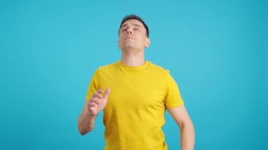 Stüdyoda soğuk hapşıran ve burnunu silen bir adamın mavi arka planlı videosu var.