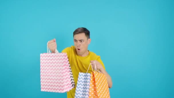 视频在工作室蓝色背景的一个男人跳舞和微笑与购物袋 框架开始是空的 男人从下面出现 然后消失在底部 — 图库视频影像