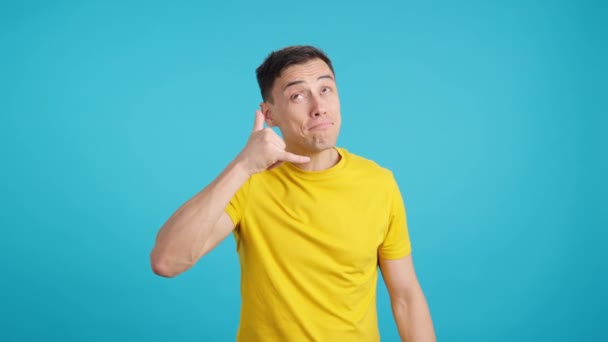 笑顔の男のジェスチャーの青い背景を持つスタジオでのビデオ彼の指で呼び出しを行うために招待 — ストック動画