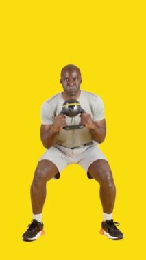 Stüdyoda, sarı arka planda bir Afrikalı sporcunun kettlebell ile iki kez çömeldiği bir video var.