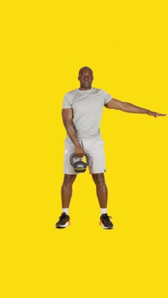 ビデオでスタジオともに黄色の背景のスポーツアフリカ人男あります行演習とともに1つのKettlebel — ストック動画