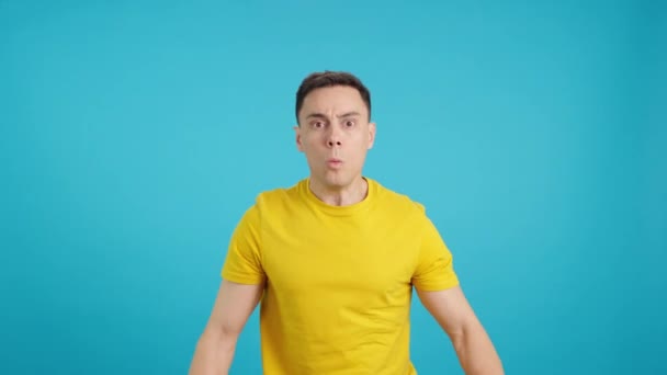 コミカルな表情をした男の青い背景を持つスタジオでのビデオは驚きで彼の目を開きます — ストック動画