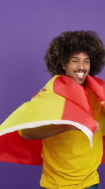 Afrikalı bir adam stüdyoda İspanyol bayrağıyla kameraya gülümsüyor.