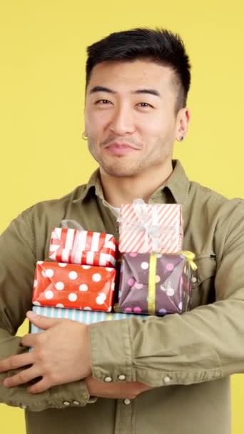 Щасливий Китайський Чоловік Ховає Багато Барвистих Подарунків Студії Жовтим Фоном — стокове відео