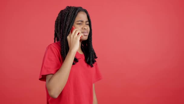 赤の背景を持つスタジオでモバイルと話す怒っているアフリカの女性 — ストック動画