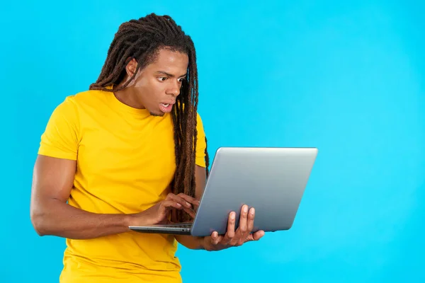 stock image Surprised latin man with dreadlocks using a laptop in studio with blue background