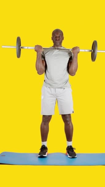带黄色背景的工作室里的视频一个非洲男人带着举重棒做卷曲二头肌 — 图库视频影像