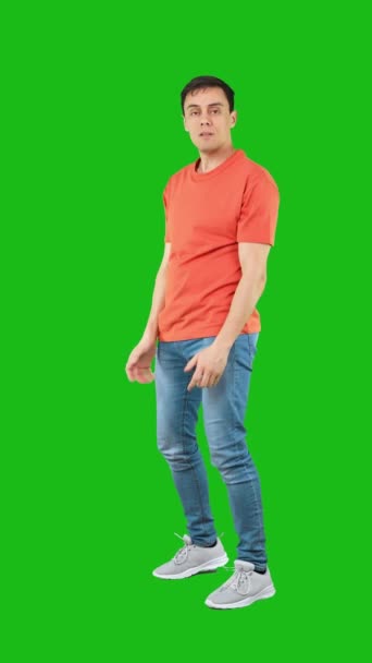 フルボディ怒っている男でジーンズとオレンジTシャツ見ますカメラ積極的にと持ち上げるクリーンな拳のためにパンチ隔離された緑の背景 — ストック動画