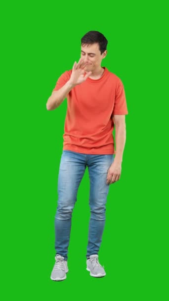 全身上下都是自信而积极的男青年 穿着深色的T恤和牛仔裤 在智能手机上站在绿色背景下开心地笑着 — 图库视频影像