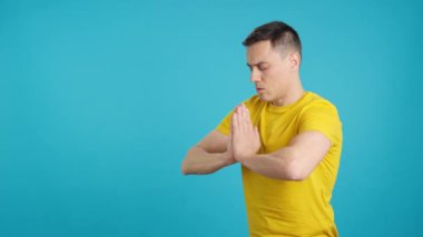 Meditasyon yaparken derin nefes alan bir adamın mavi arka planlı videosu stüdyoda.