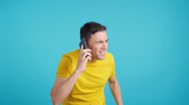 Cep telefonundan duyduklarını dinlemeye çalışan bir adamın mavi arka planlı videosu stüdyoda.