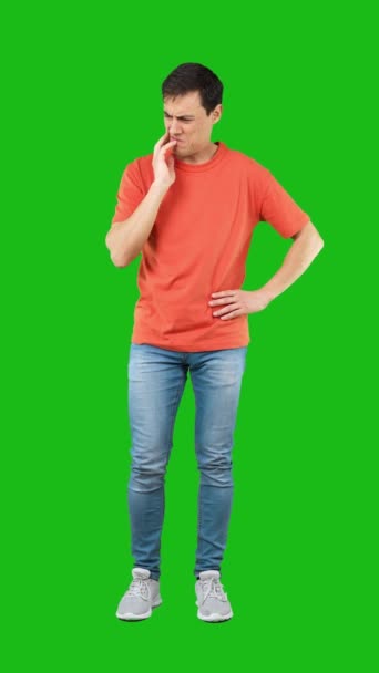 シャツとジーンズの若い不確実な男の完全な長さは肩を振り 緑の背景に対して混乱した顔の表情を作ります — ストック動画