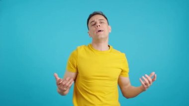 Stüdyoda mavi arka planda yetişkin bir adamın kaba hareketler yaptığı bir video var.