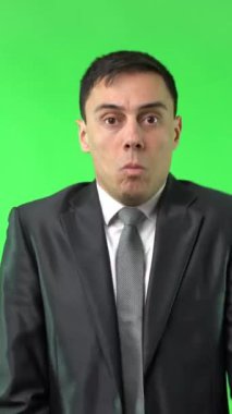 Korkak genç girişimci, koyu renk saçlı, resmi kıyafetli yüzünü kapatan ve kroma anahtarına karşı kameraya bakan.