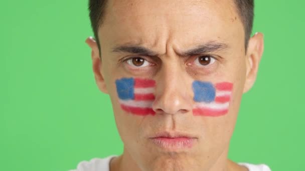 カメラを見ている顔に描かれたアメリカの国旗を持つ深刻な男のクロマのスタジオでのビデオ — ストック動画