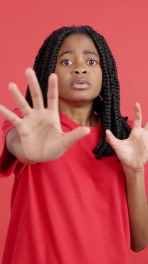 Korkmuş Afrikalı kadın elleri korku içinde stüdyoda kırmızı arka planda el kol hareketi yapıyor.