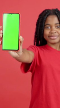 Stüdyodaki kırmızı arka planı olan Afrikalı kadının cep telefonunun boş ekranı.