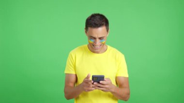 Yüzünde Ukrayna bayrağı olan ve cep telefonuna bakıp gülümseyen ve ekranı krom tuşlu gösteren Ukraynalı bir adamın krom arka planına sahip bir stüdyo videosu..