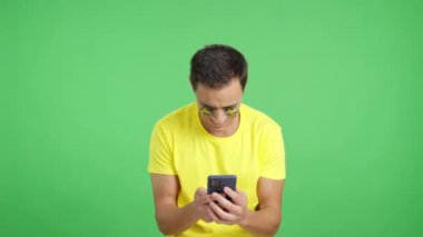 Yüzünde İsveç bayrağı olan İsveçli bir destekçinin krom arka planına sahip bir stüdyo videosu, cep telefonuna bakıp gülümsüyor ve onu krom tuşlu ekranla kameraya gösteriyor.