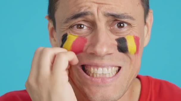 在演播室里用彩色的特写拍摄了一个非常紧张的男人 他的脸上挂着一面比利时国旗 在一场最后以失败告终的艰难的比赛中 他支持着一支比利时球队 — 图库视频影像