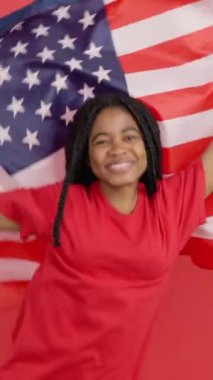 Stüdyoda kırmızı arka planda Kuzey Amerika bayrağını göndere çeken mutlu Afrikalı kadın