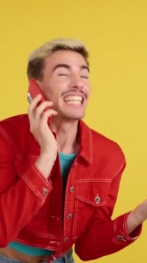 Stüdyoda sarı arka planda cep telefonuyla konuşurken eşcinsel adam kutlama yapıyor.