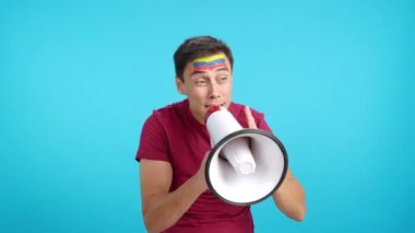 Stüdyoda, yüzünde Venezuela bayrağı olan bir adamın krom rengiyle kalabalığı megafonla canlandıran bir video.