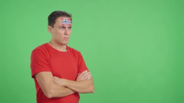 Stüdyoda, yüzünde Norveç bayrağı olan bir adamın ciddi bir ifadeyle bakışlarını çevirdiği bir video.