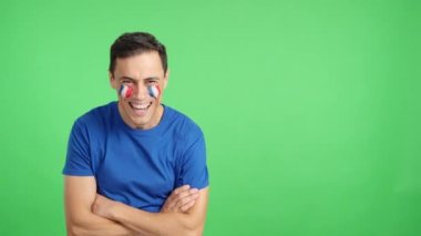 Stüdyoda, yüzünde Fransız bayrağı olan kollarını kavuşturarak gülümseyen bir adamın kromasıyla.