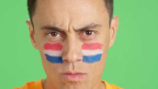 カメラを見ている顔に描かれたオランダの旗を持つ深刻な男のクロマのスタジオでのビデオ — ストック動画