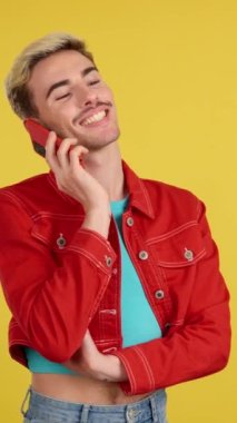 Stüdyoda cep telefonuyla konuşurken gülümseyen eşcinsel adam sarı arka planda.