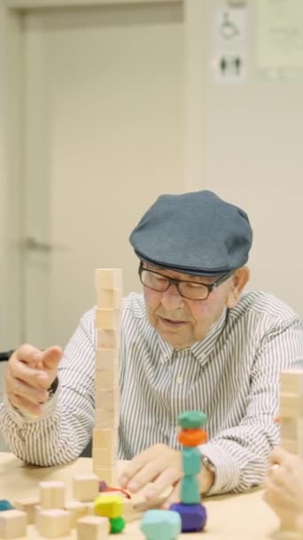 高齢者のスキルゲームとして木製のタワーを構築する男のビデオ — ストック動画