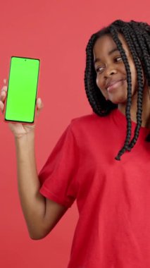 Stüdyoda kırmızı arka planda krom ekranlı cep telefonu tutan mutlu Afrikalı kadın.