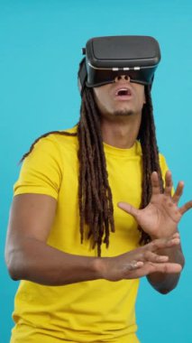 Rastalı mutlu Latin adam stüdyoda mavi arka planlı sanal gerçeklik gözlüğü takıyor.