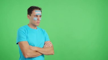 Stüdyoda, yüzünde Arjantin bayrağı olan bir adamın ciddi bir ifadeyle yüzünü boyadığı bir video.