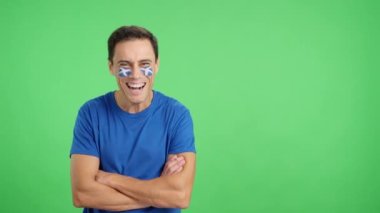 Stüdyoda, yüzünde İskoç bayrağı olan kollarını kavuşturmuş gülümseyen bir adamın kromasıyla.