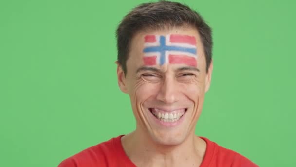 摄影棚里的录像 彩色的是一个男人的特写 他的脸上挂着一面挪威国旗 对着摄像机微笑 — 图库视频影像