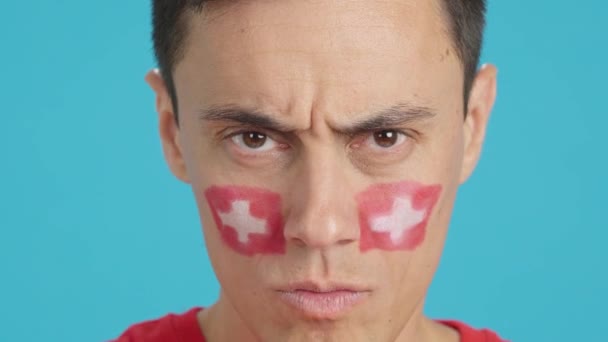 摄影棚里的录像 彩色的是一个严肃男子的特写 他的脸上挂着一面瑞士国旗 看着镜头 — 图库视频影像