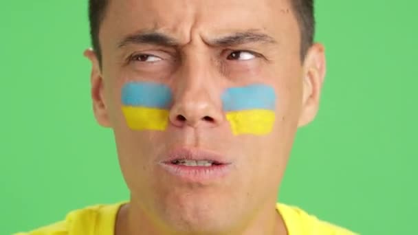 在演播室里用彩色照片近距离拍摄一个脸上挂着乌克兰国旗的非常紧张的男人 他在比赛中支持乌克兰球队 但这场比赛最终以失败告终 — 图库视频影像